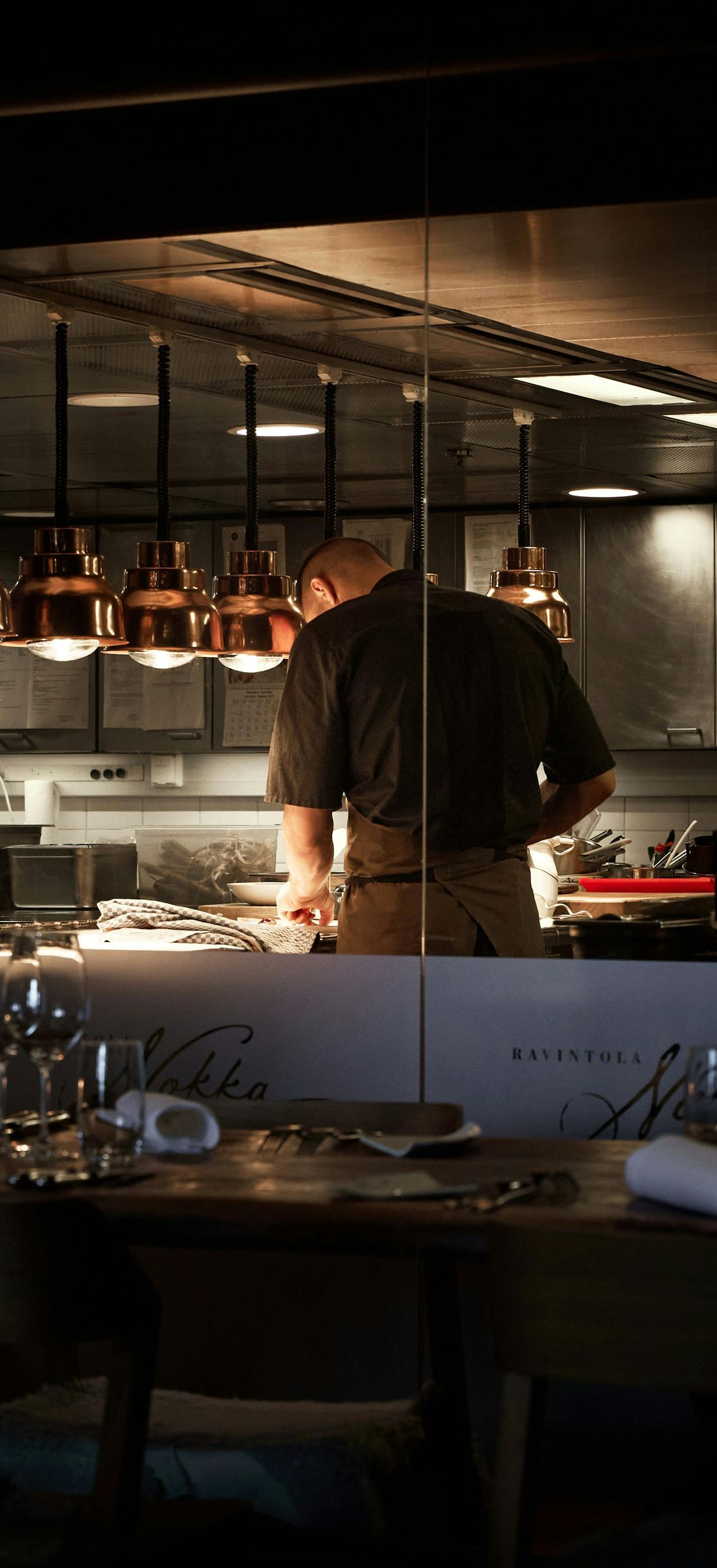 Chef working in a warm-lit restaurant kitchen beside hanging copper pans