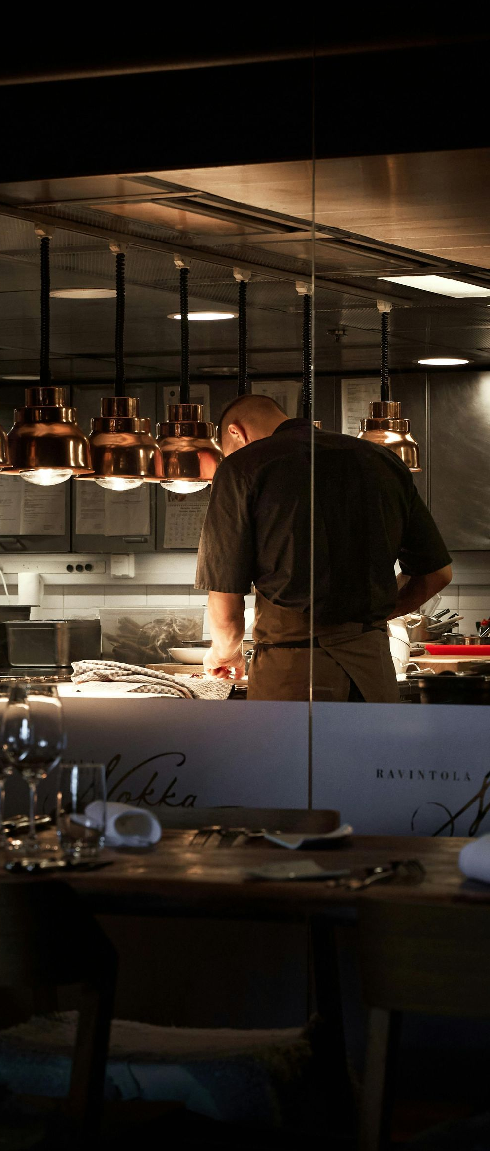 Chef working in a warm-lit restaurant kitchen beside hanging copper pans