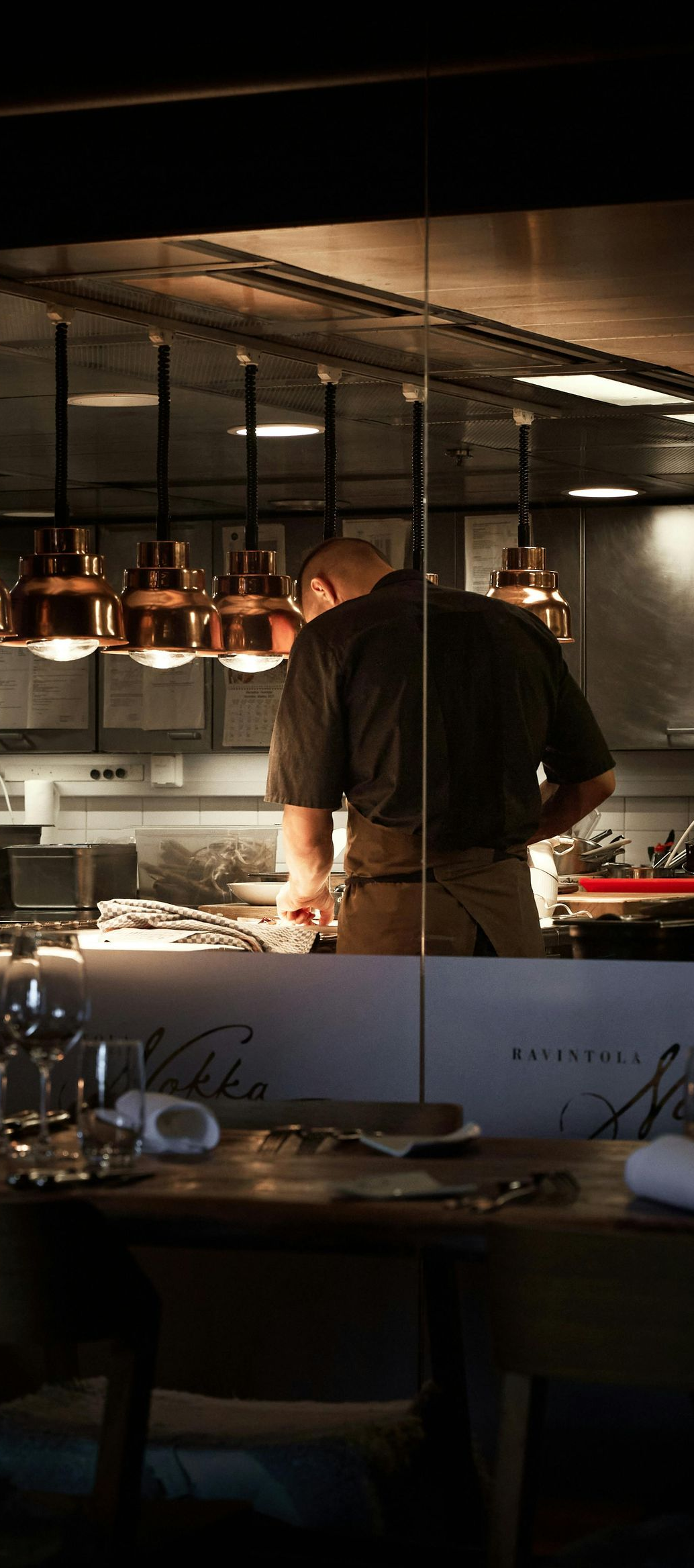 Chef working in a warm-lit restaurant kitchen beside hanging copper pans
