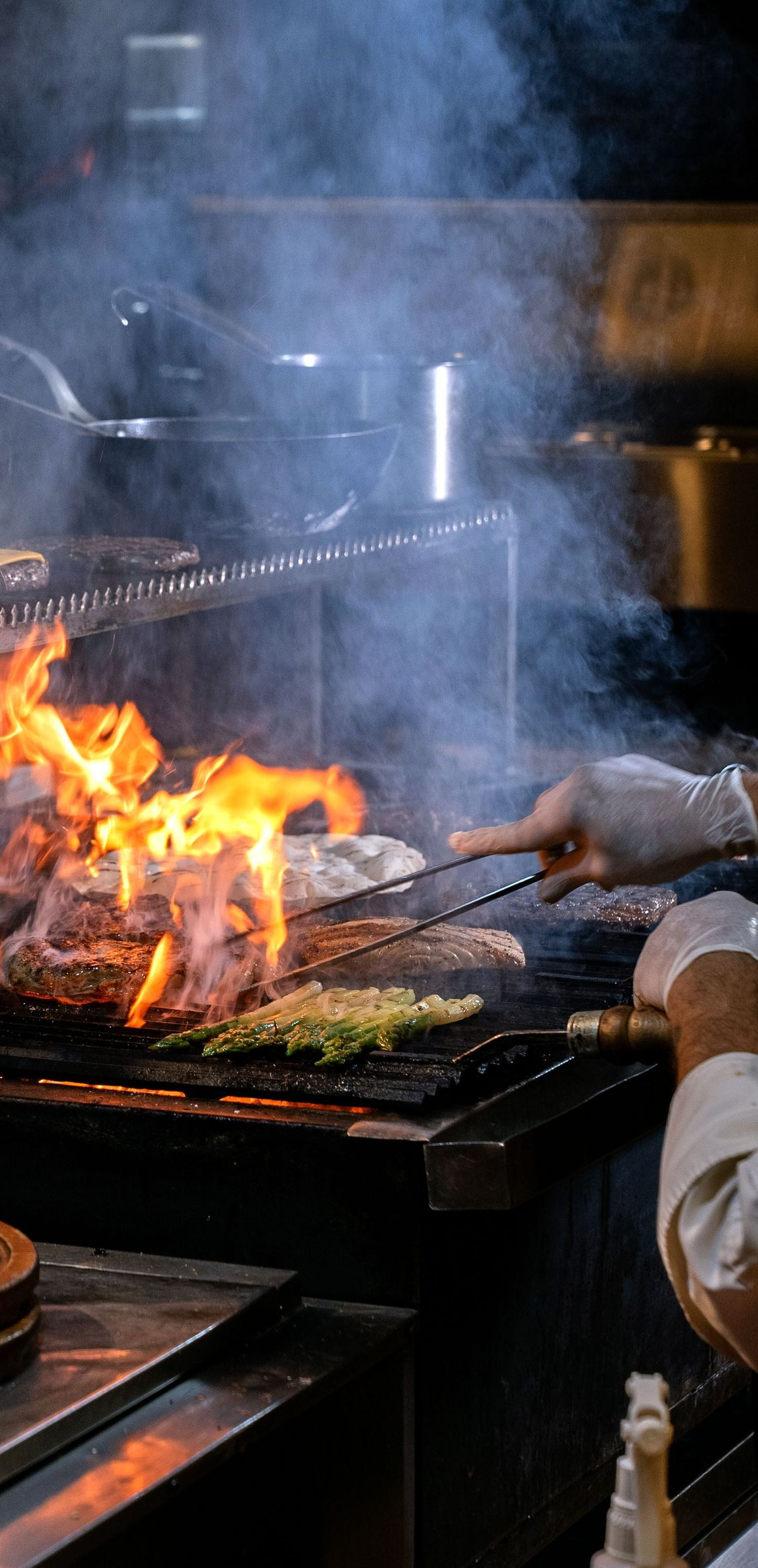 Chef grilling vegetables over open flames in a smoky kitchen