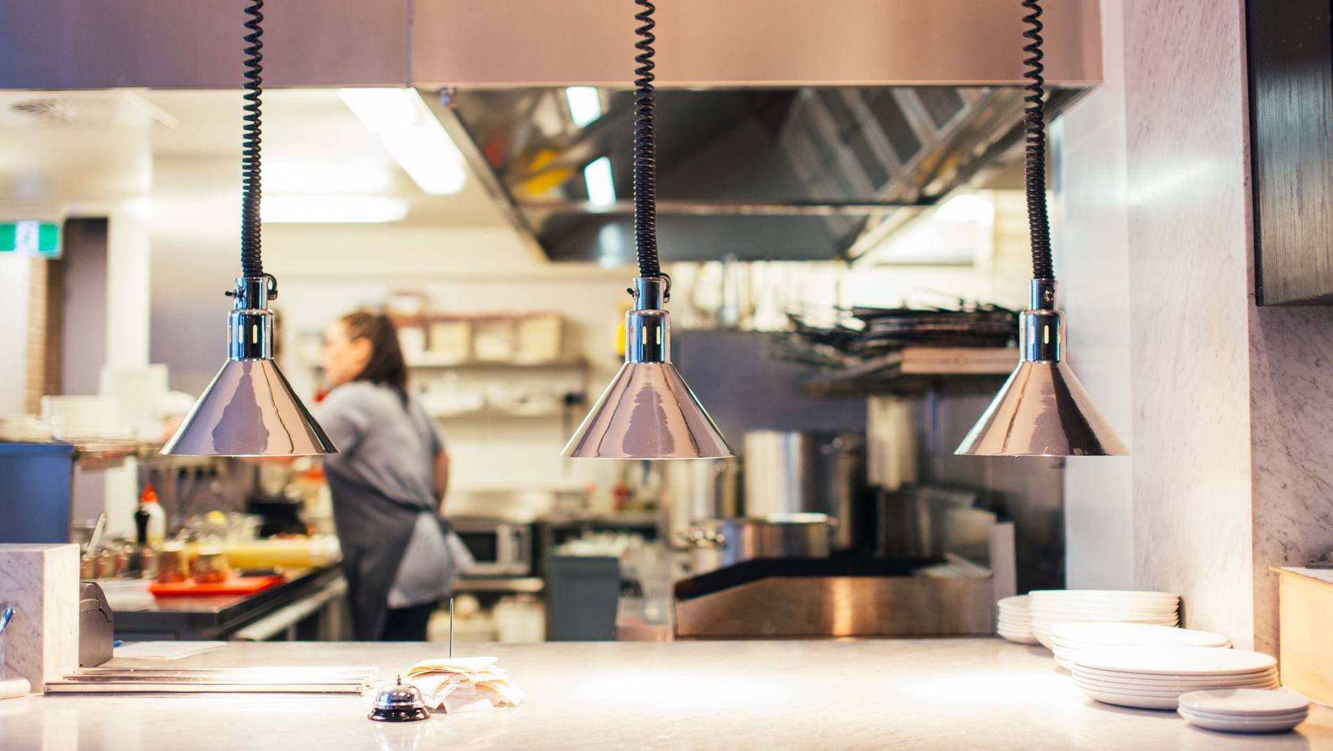 Open restaurant kitchen with hanging heat lamps and a chef working behind the counter