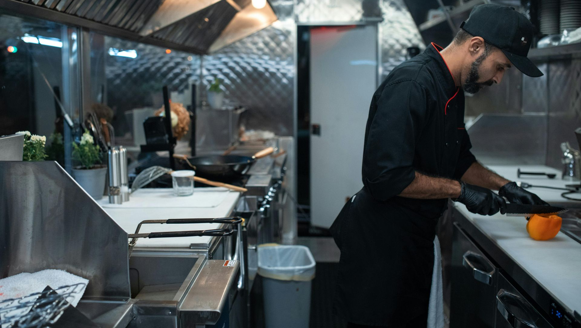 Chef in black uniform prepping food inside a food truck kitchen, stainless steel counters.