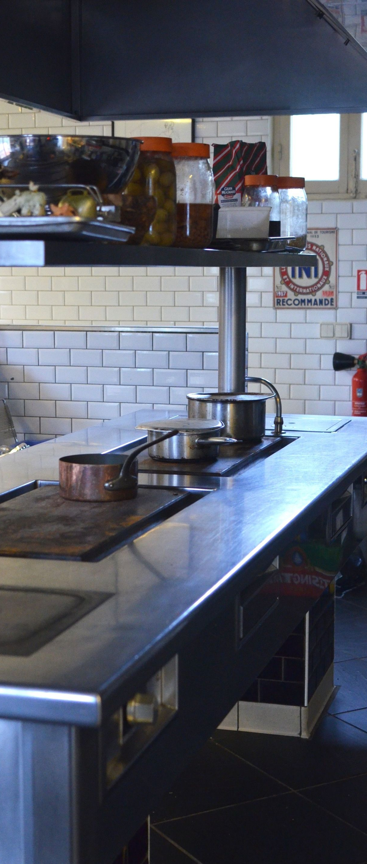 Stainless-steel kitchen with counters, pots, shelves, and white subway tile walls
