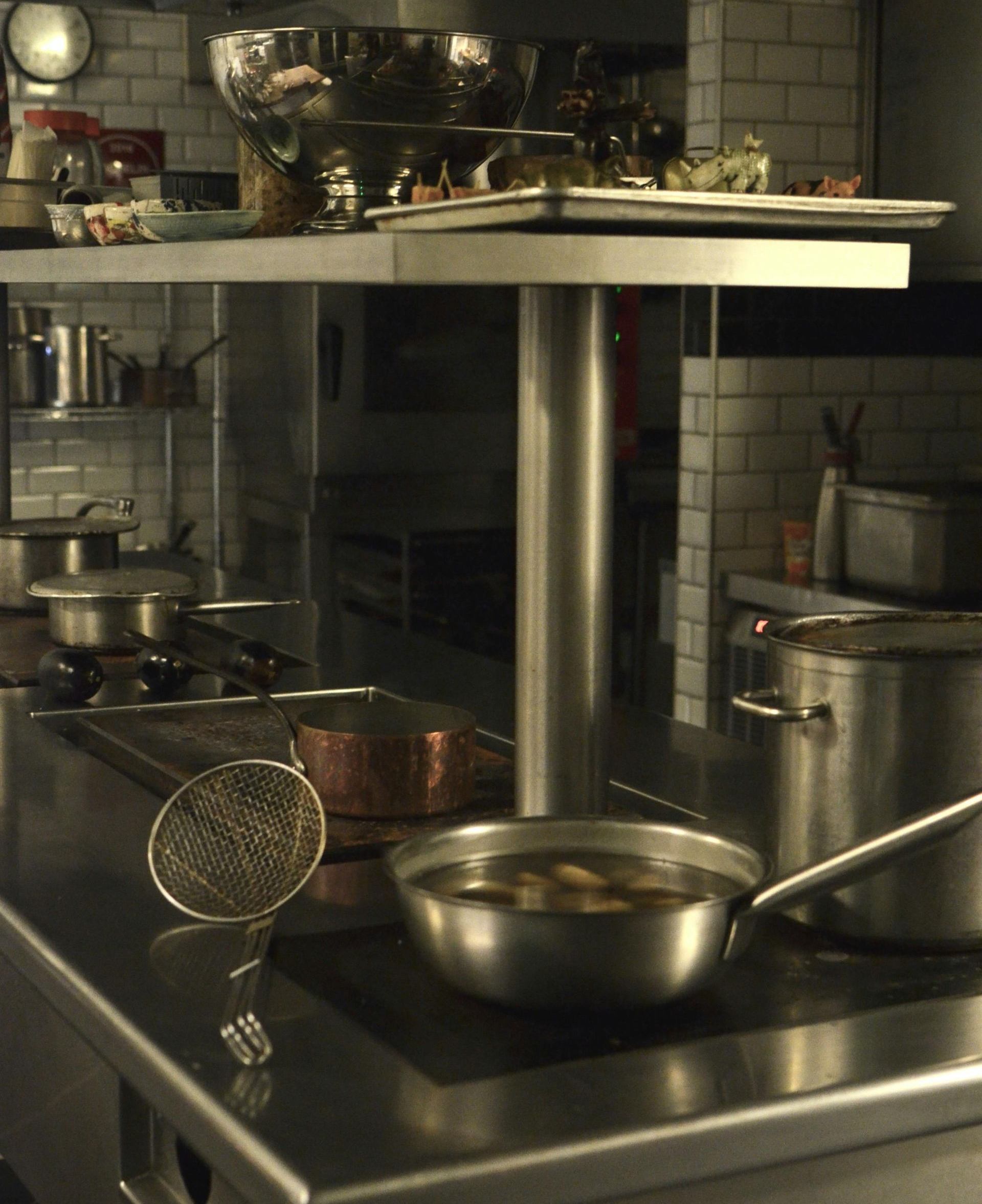 A commercial stainless steel kitchen prep station with pots, a metal strainer, and cookware on a stove.