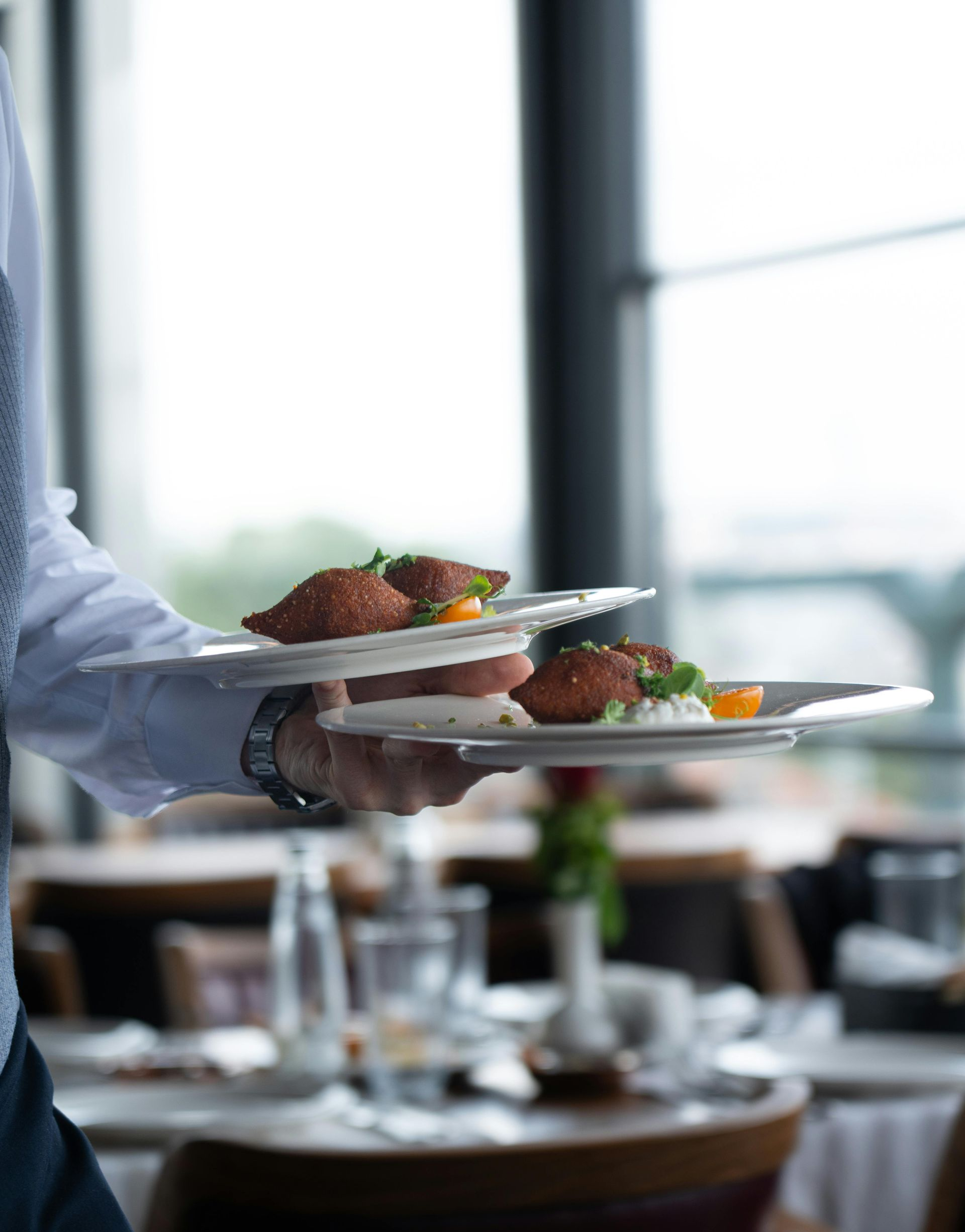 Server carrying plates of food in a bright restaurant dining room