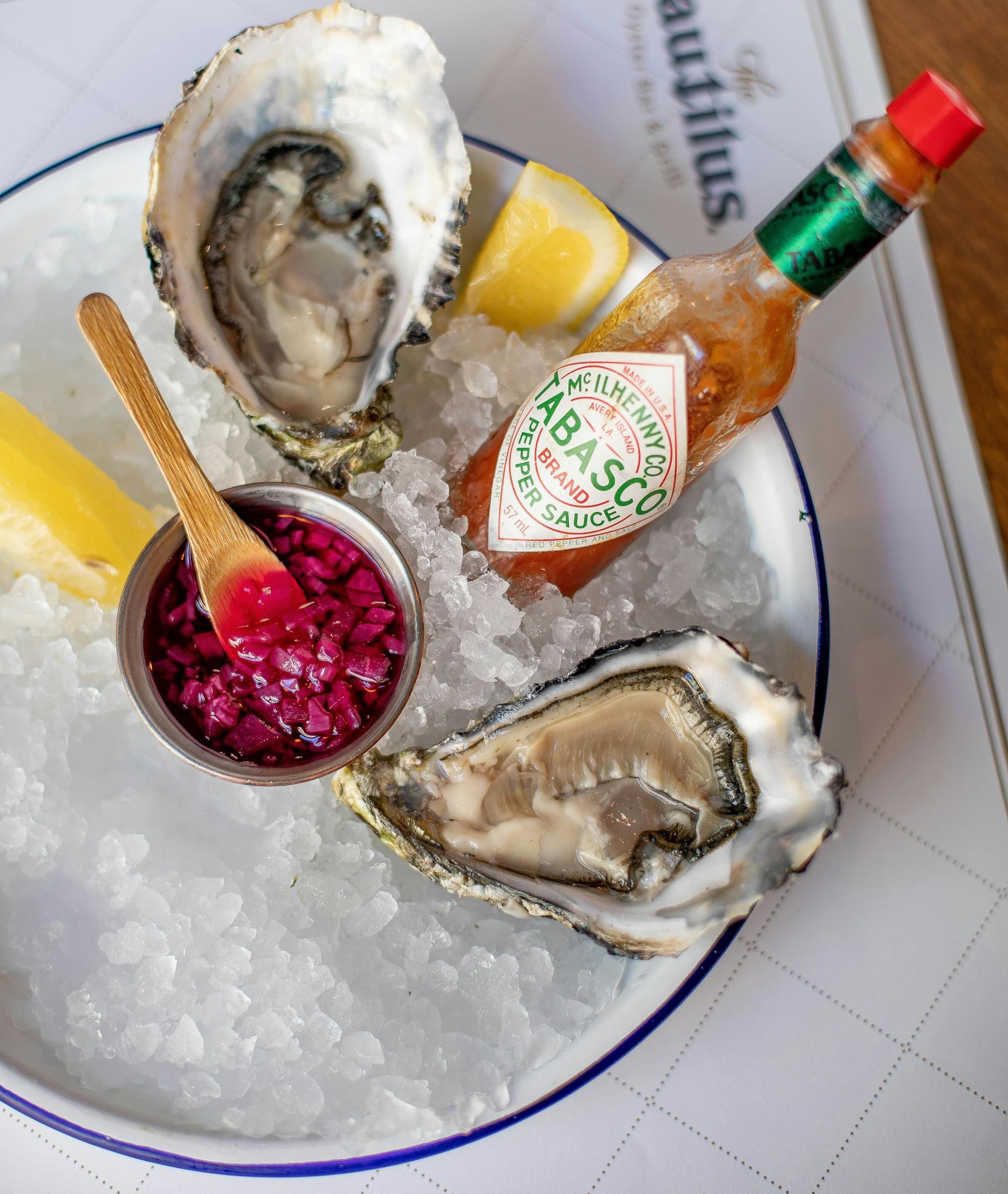 Oysters on ice with lemon wedges, Tabasco sauce, and a small bowl of red sauce.