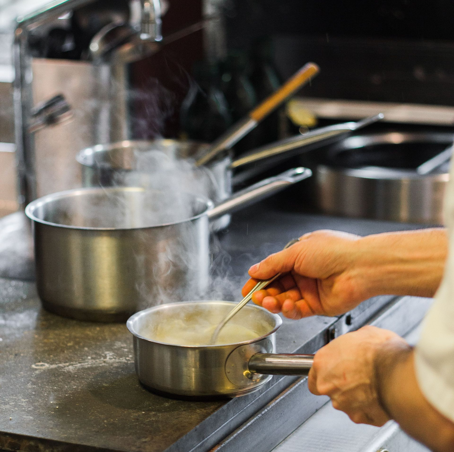 Person stirring sauce in a saucepan on a stove in a kitchen