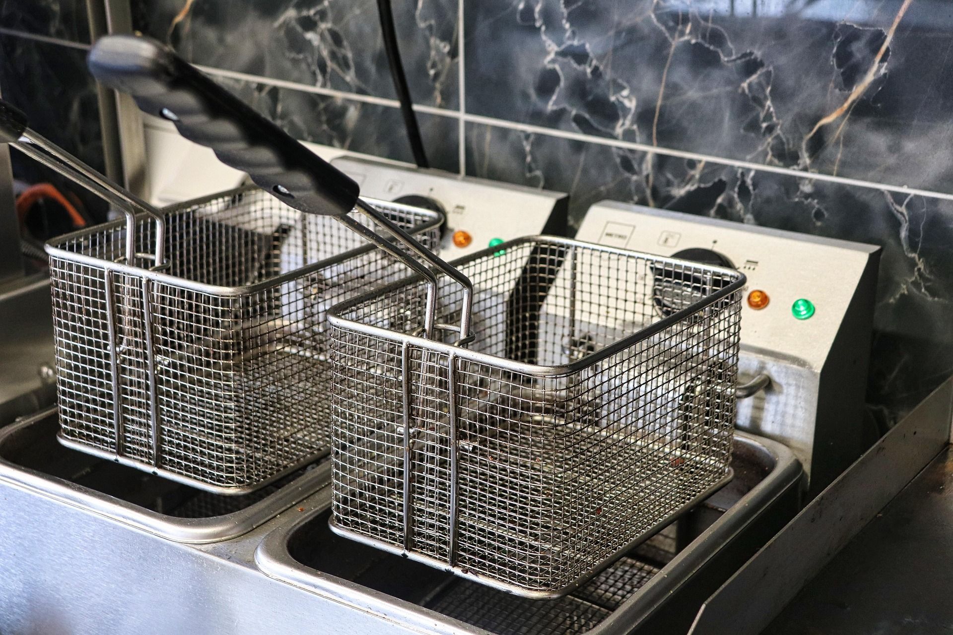 Twin wire fryer baskets in a commercial kitchen, with black handles over a stainless steel sink.