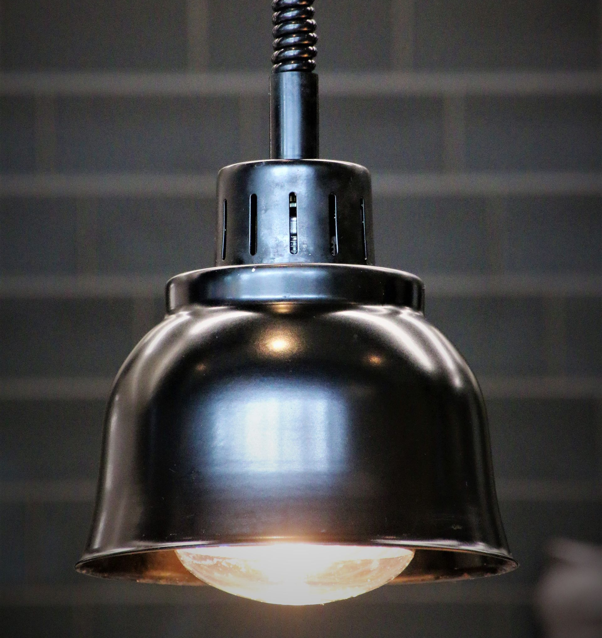 Chrome pendant light hanging from a ceiling, glowing softly against a brick wall.