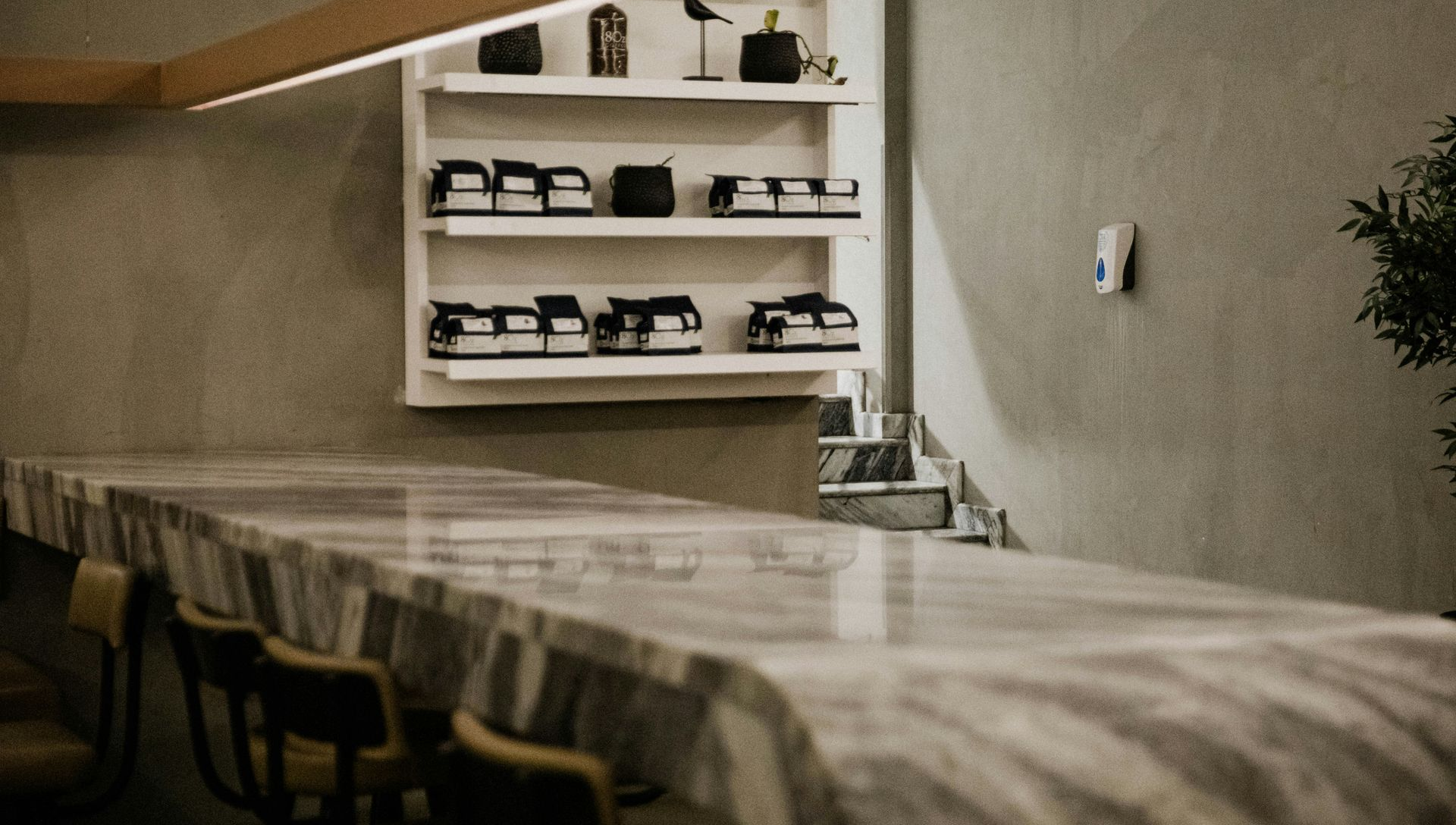 A long marble table in a minimalist room with gray walls and shelves displaying products and decor items.