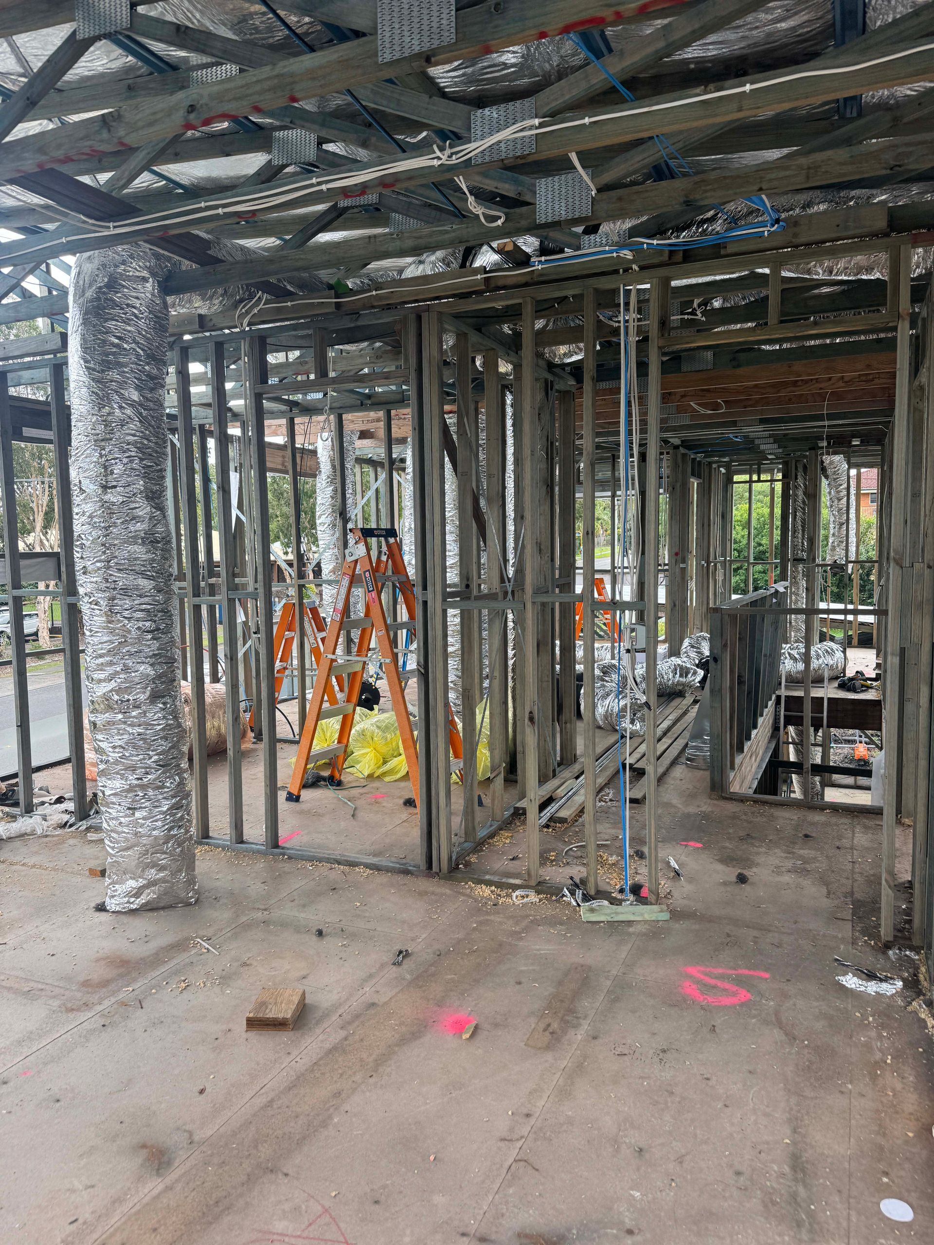 Interior view of a building under construction. Wooden framing, exposed ductwork, and insulation are visible.