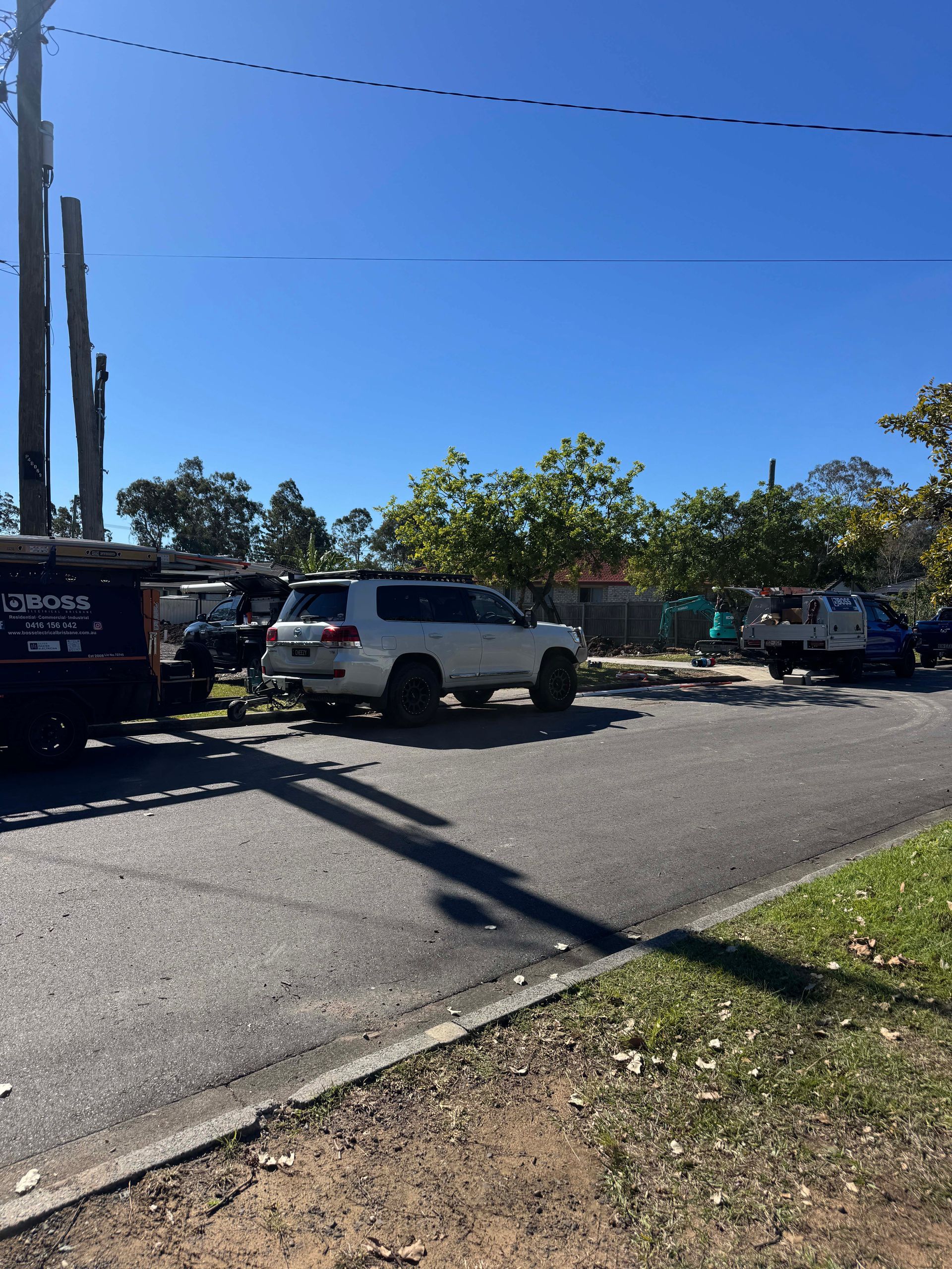 A white SUV parked on a street near construction equipment. The sky is blue, and the setting appears to be residential.