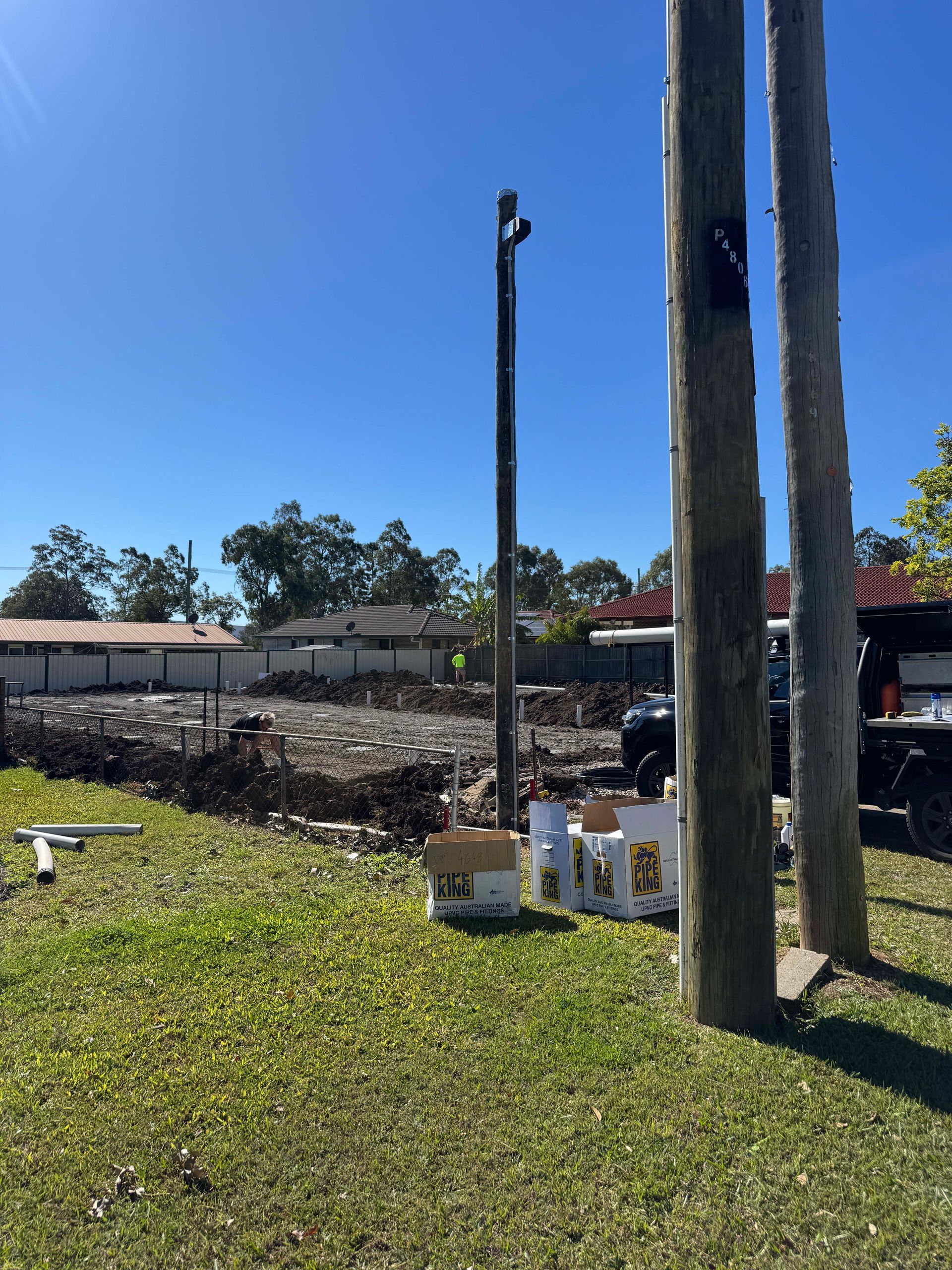 Lawn with power poles and a tall, dark pole with a camera. Construction in background, sunny day.