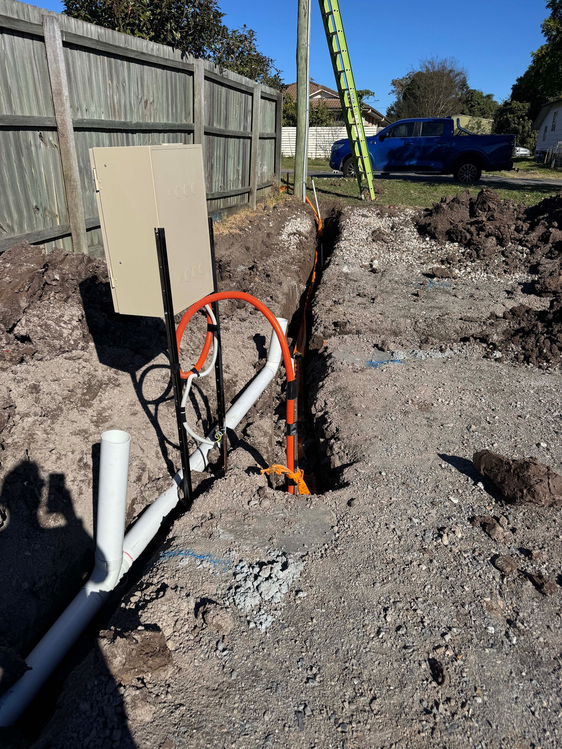 Construction site with an open trench revealing electrical and plumbing work in progress.