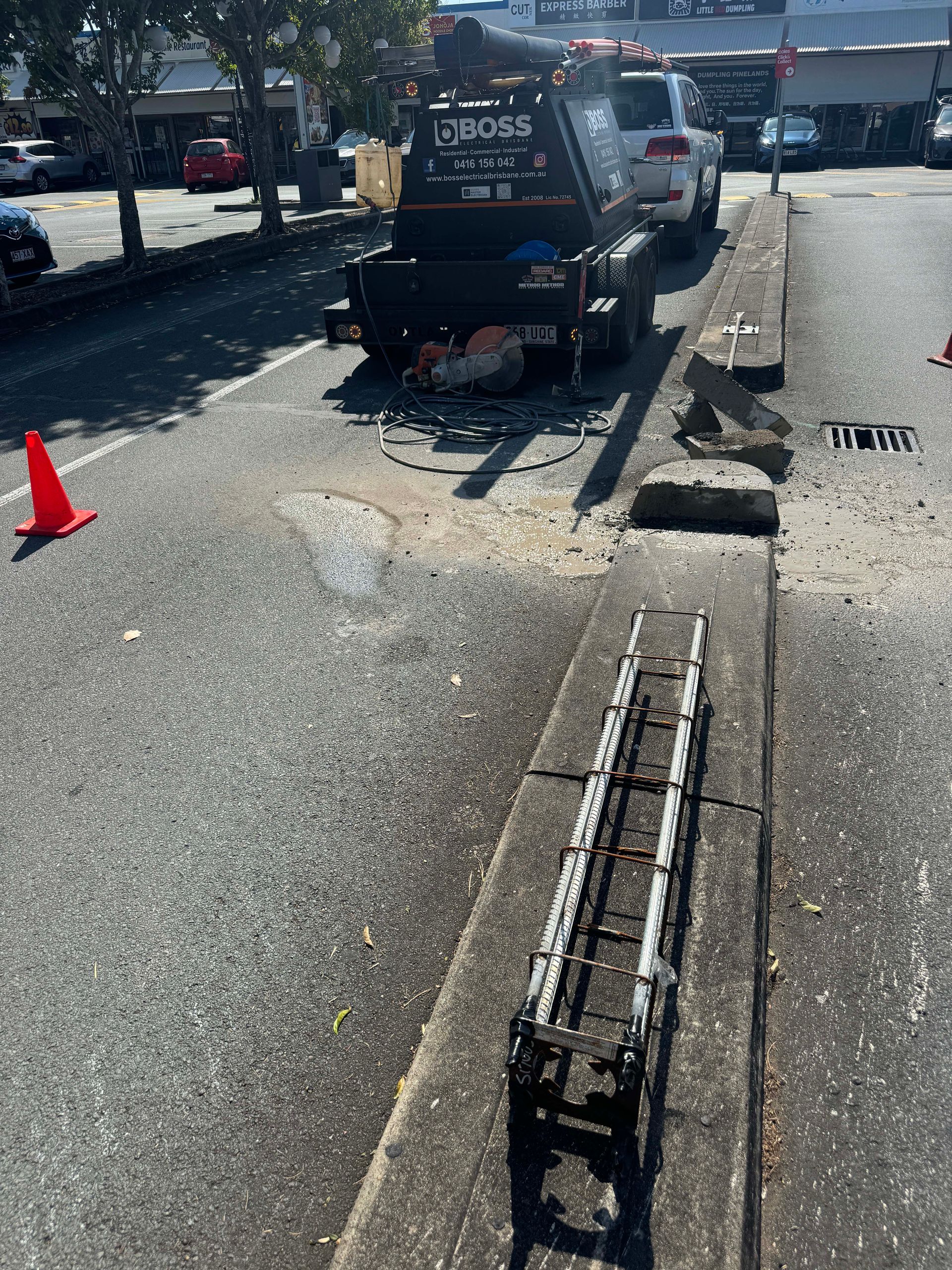 A black dump truck is parked in the street next to a concrete barrier. Debris and a ladder are in view.