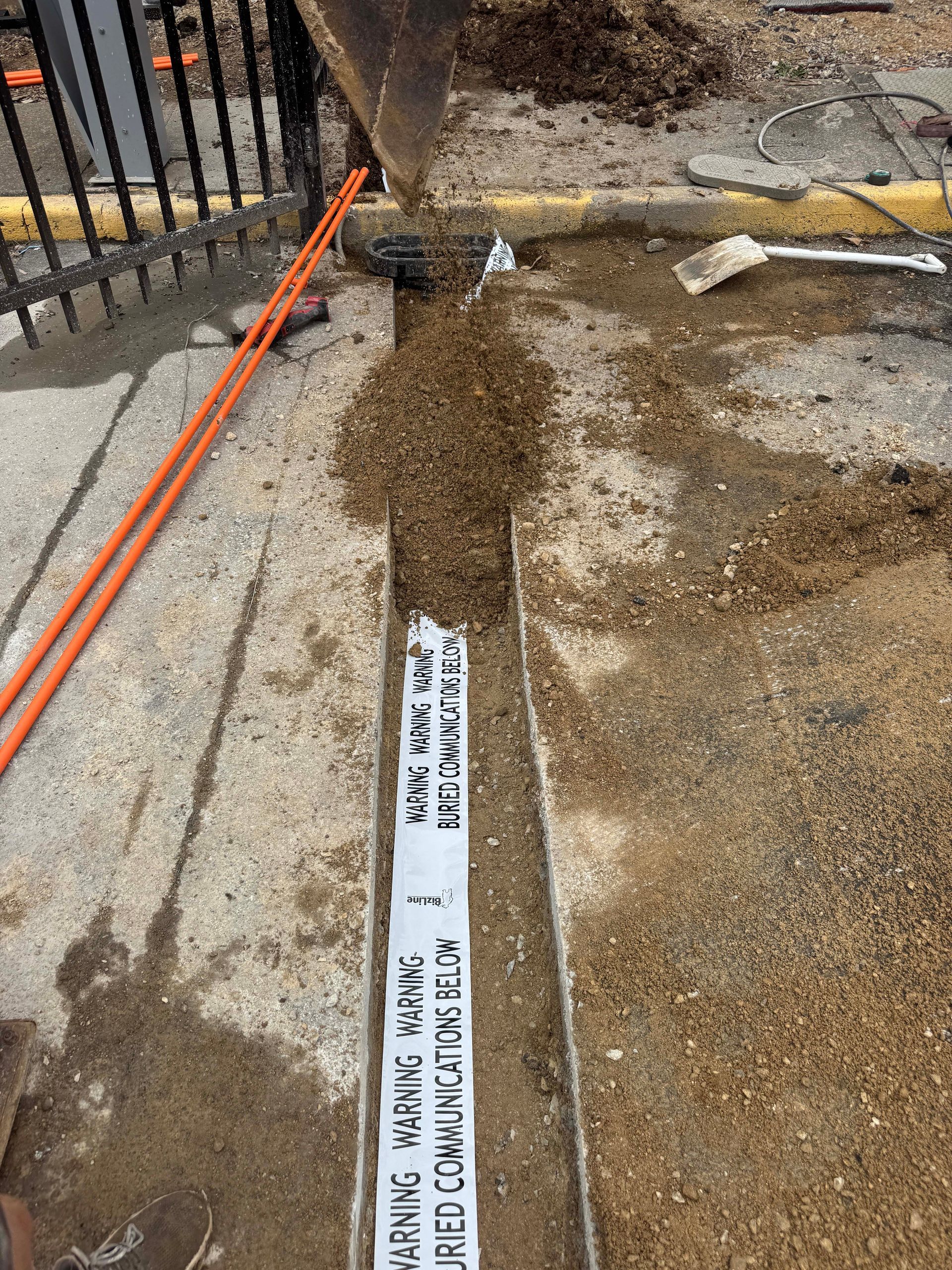 Construction site with a trench dug into concrete. Warning tape reads 