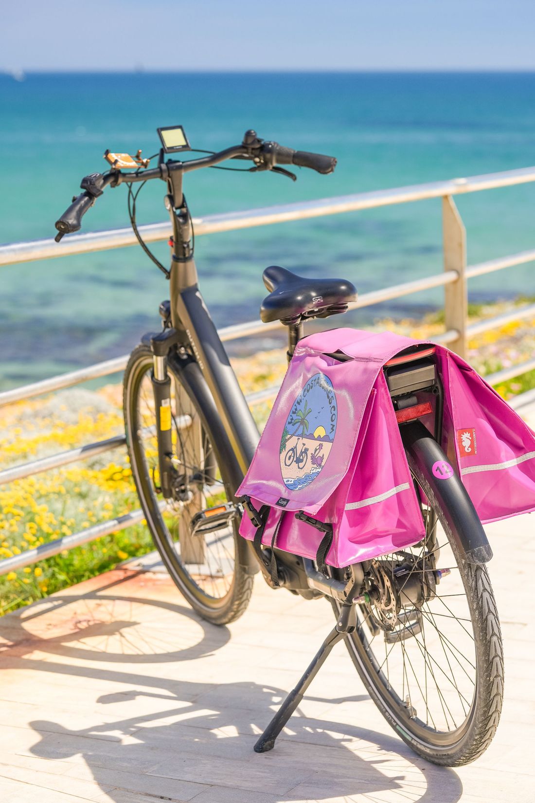 Een fietser met een roze jasje op een boulevard langs de kust, met uitzicht op de oceaan.