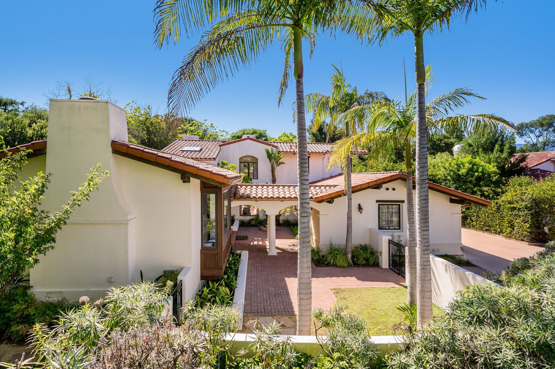 Spanish-style house with white walls, terracotta roof, and palm trees in a sunny garden