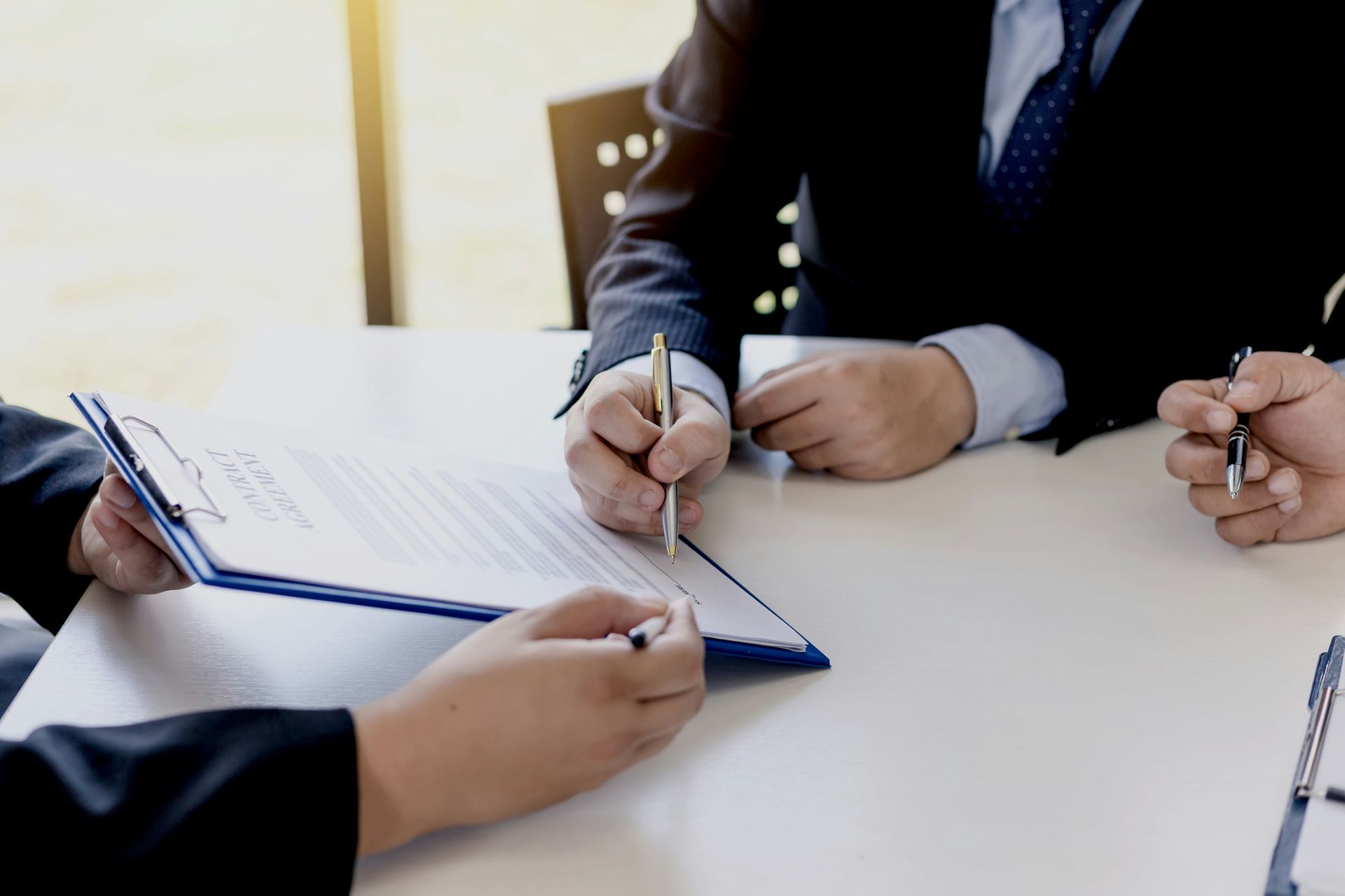 People in business attire signing a document at a table, presumably an agreement or contract.