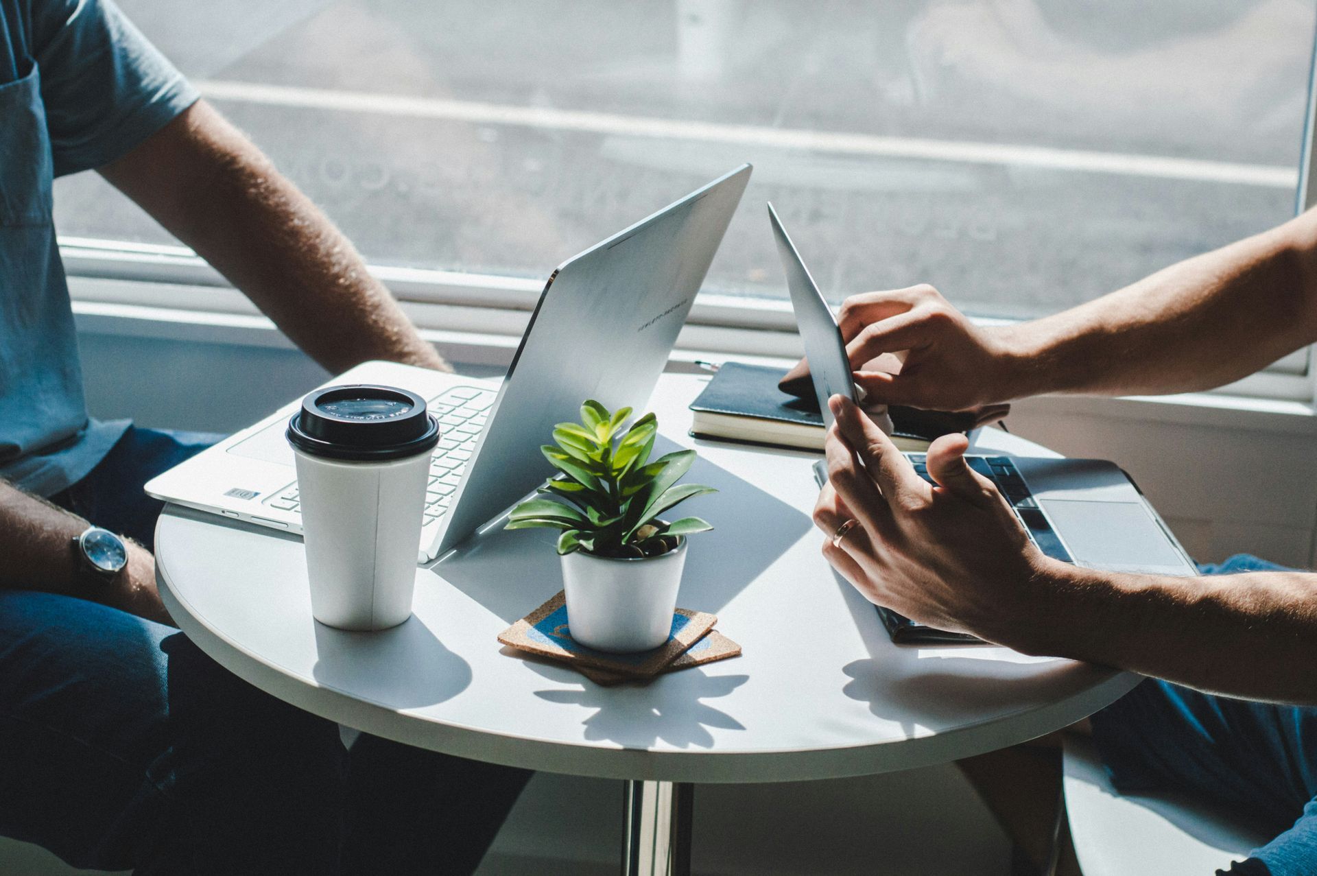 Man with glasses, writing at desk near a window. A small wind turbine model and a cup of coffee are on the table.
