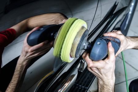 Hands using a polishing buffer on a black car door