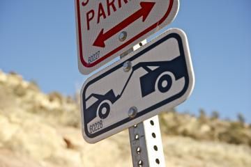 Street signs for parking and car towing, viewed against a blue sky.
