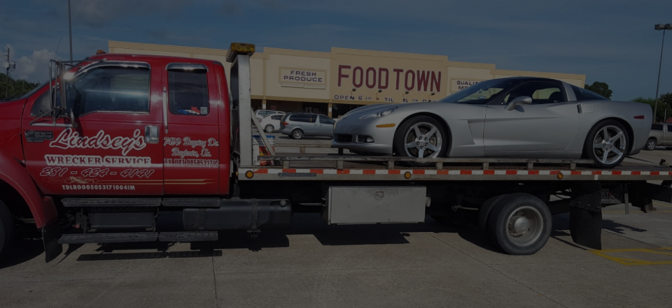 Red tow truck carrying a silver sports car in front of a Food Town sign