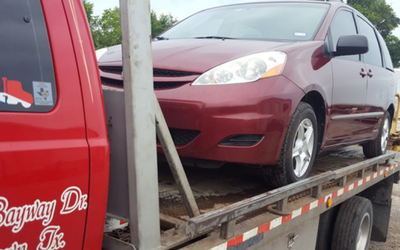 Maroon car strapped on a tow truck trailer beside a red truck.