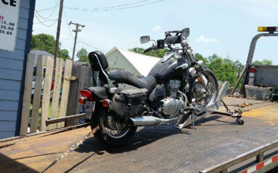 Damaged black motorcycle strapped on a flatbed tow truck on a sunny roadside
