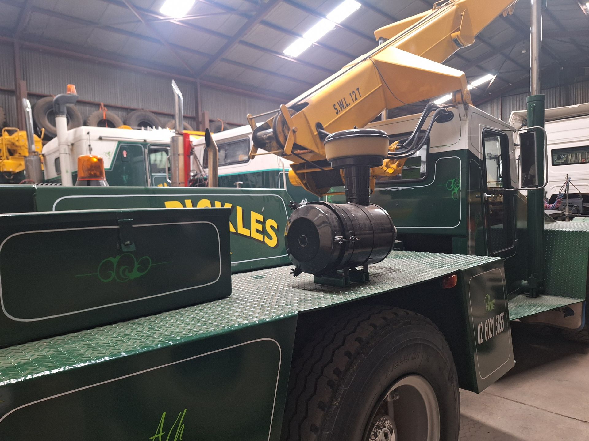 Yellow crane mounted on a green flatbed truck inside a warehouse