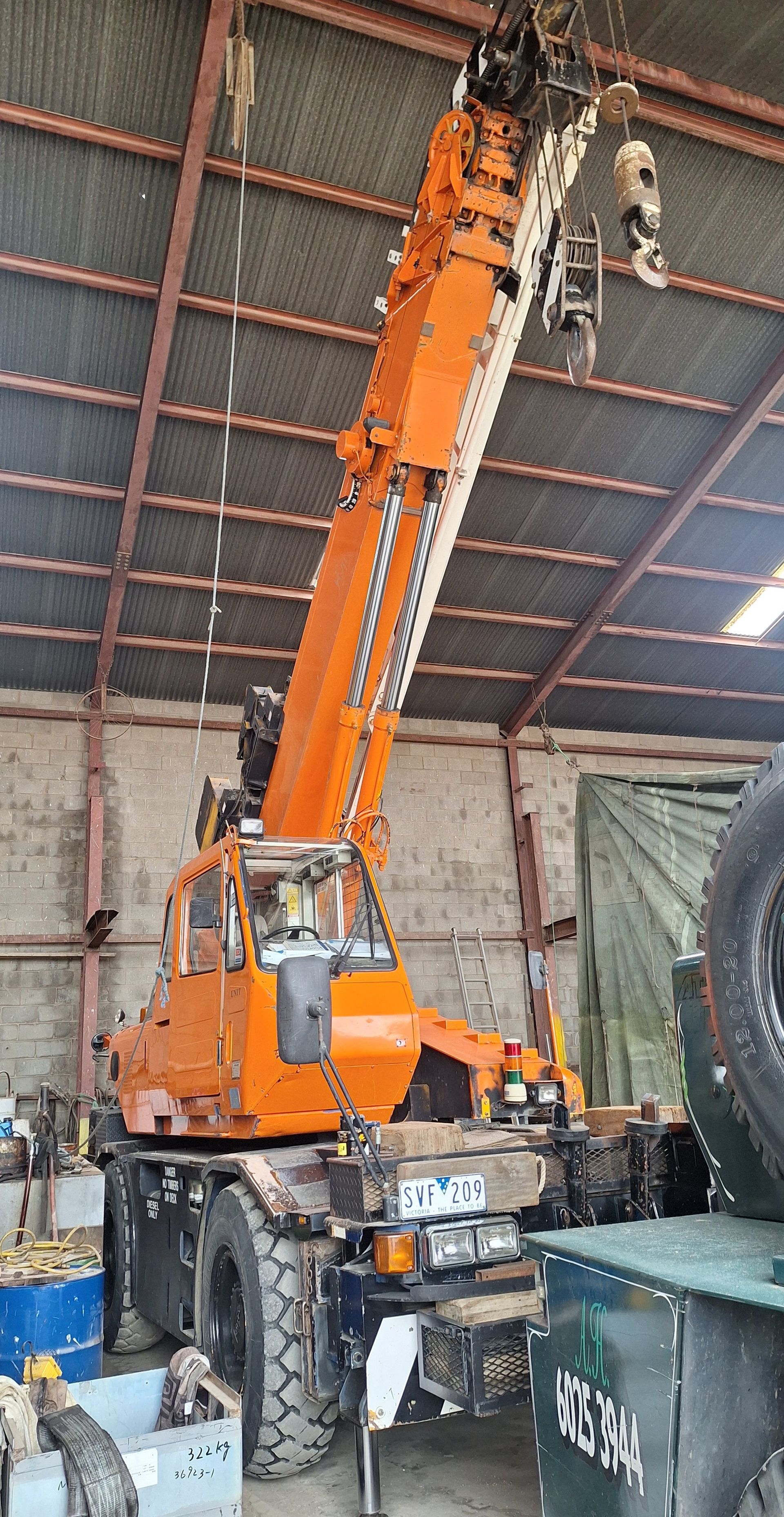 Orange mobile crane with raised boom inside an industrial warehouse with metal walls and equipment.