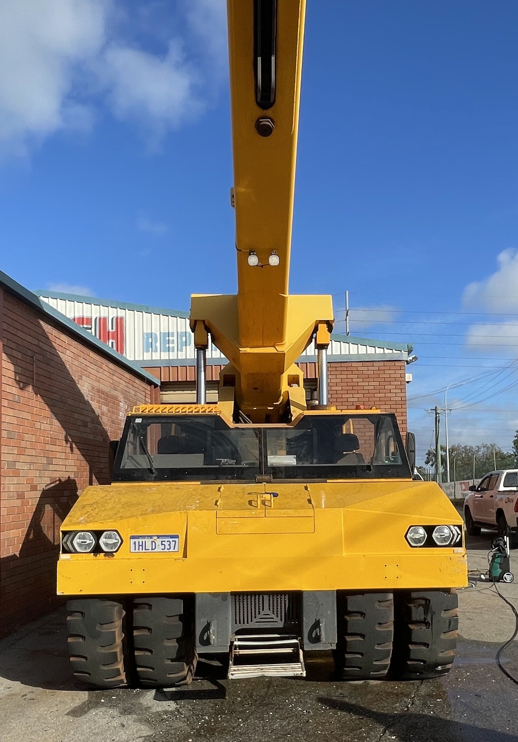 Yellow construction crane parked on a street beside a brick building under a blue sky.