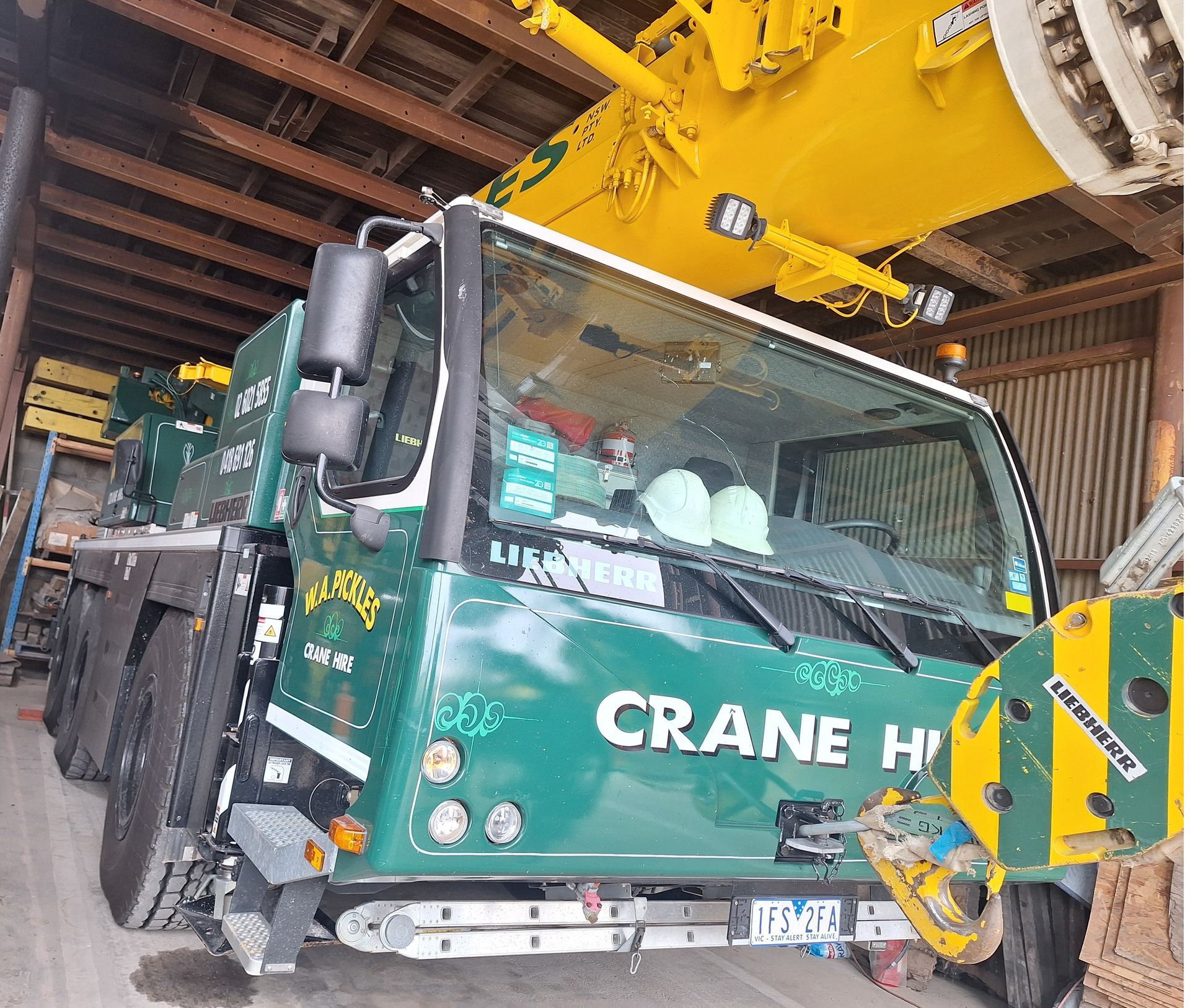 Green crane truck with a yellow boom parked inside a warehouse.