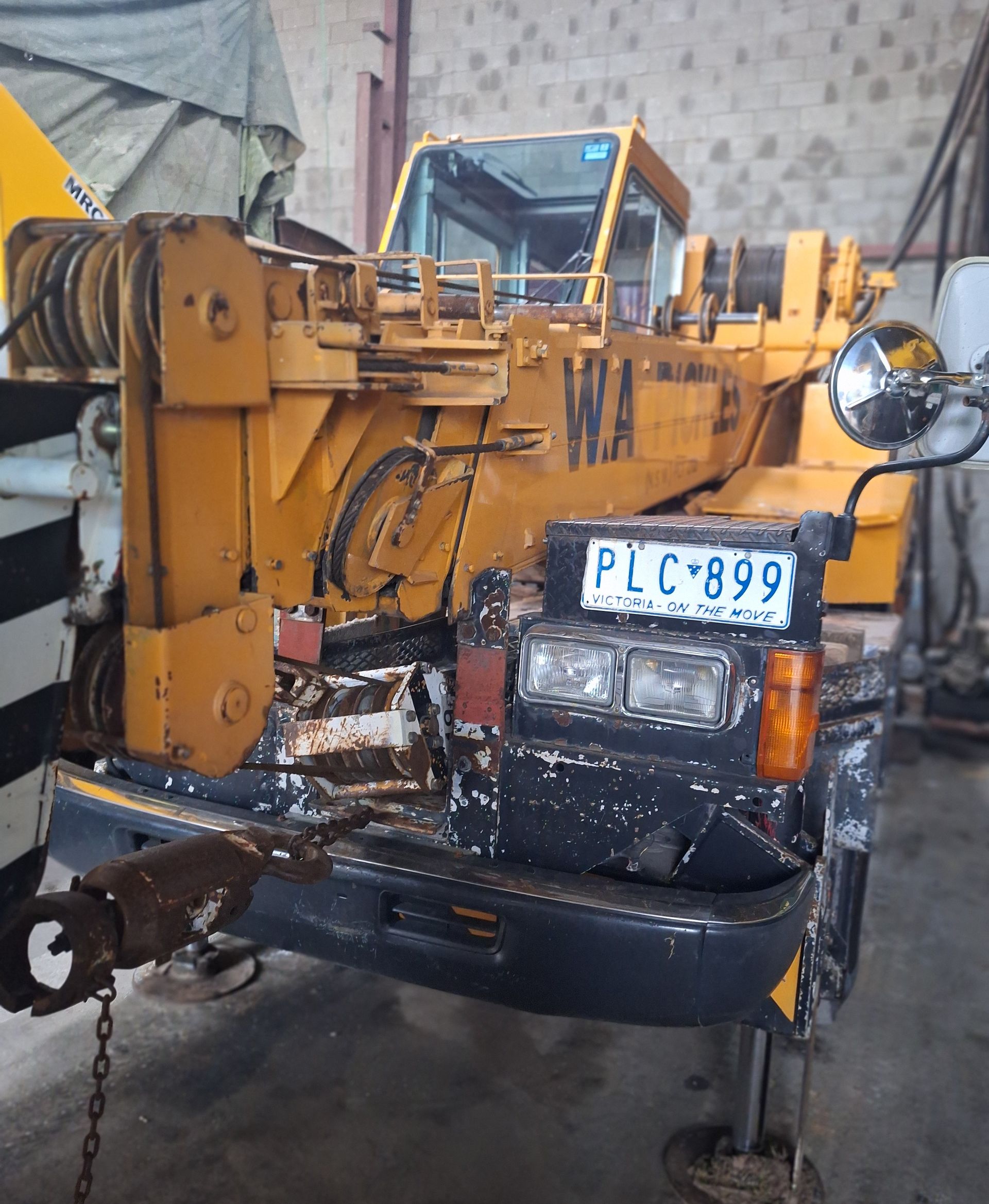 Yellow tow truck lifting a black jeepney inside a garage, with a visible license plate.