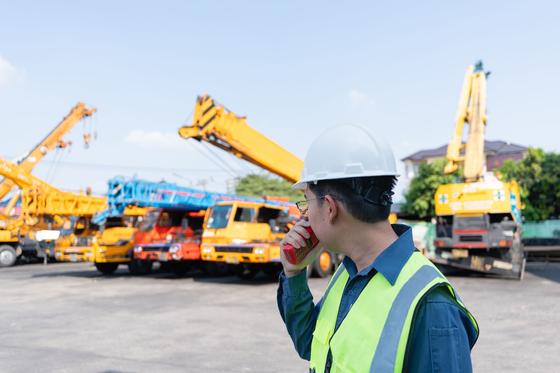 AN ENGINEER USES A RADIO BESIDES MOBILE CRANES AT A HEAVY EQUIPMENT YARD.