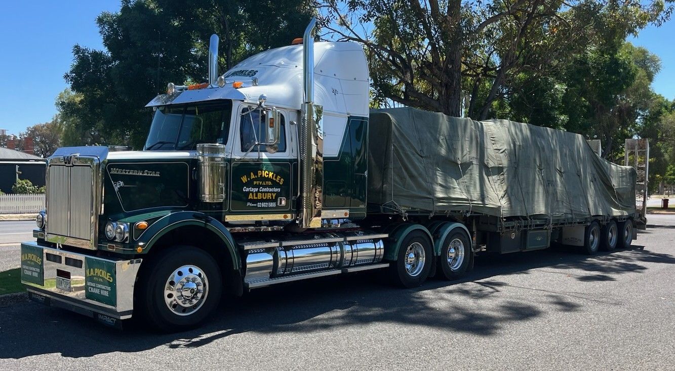 Chrome semi-truck hauling covered cargo trailers on a sunny street