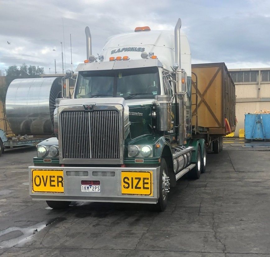 Large white semi truck with yellow “OVER SIZE” signs parked in an industrial lot.