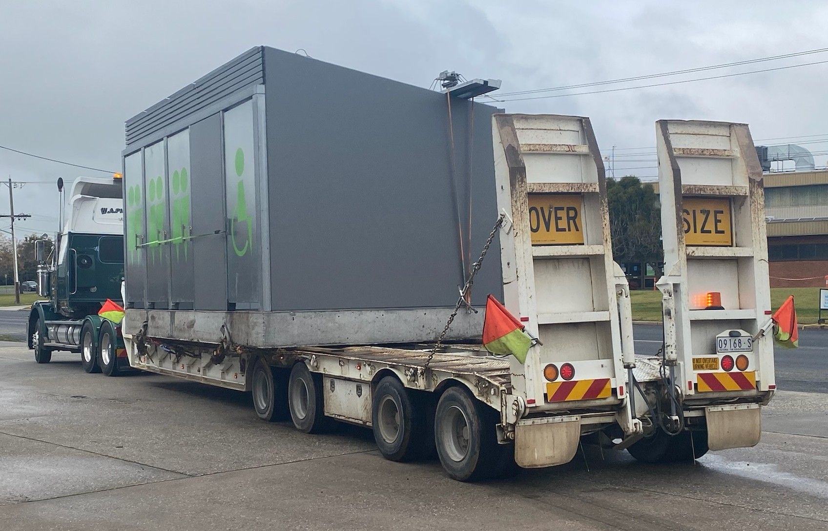 Gray truck hauling a large metal container on a wet road, with rear loading ramps visible