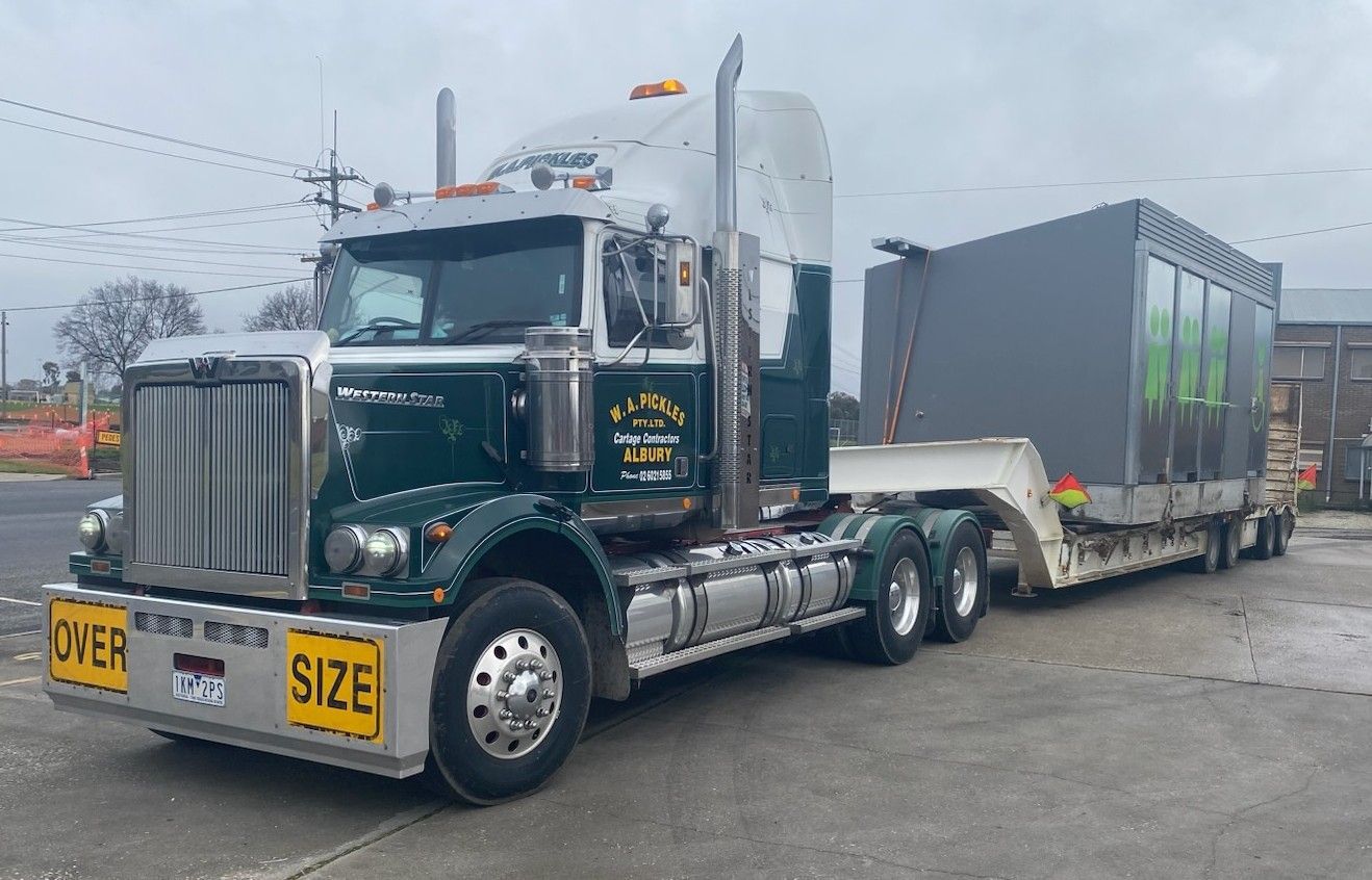 Black semi truck hauling a gray enclosed trailer on a wet roadside under overcast skies