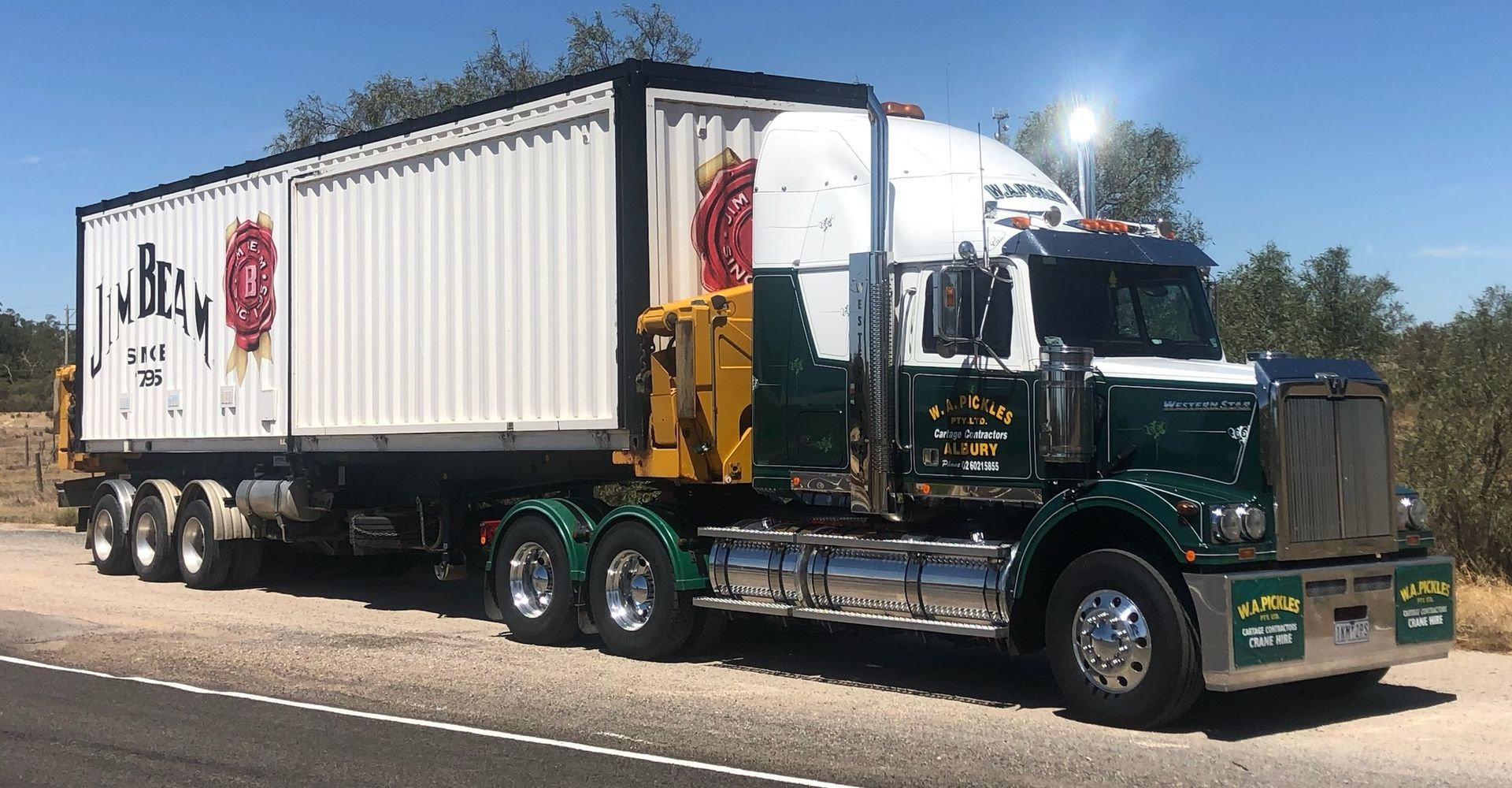 Green semi truck hauling a white refrigerated trailer on a sunny road