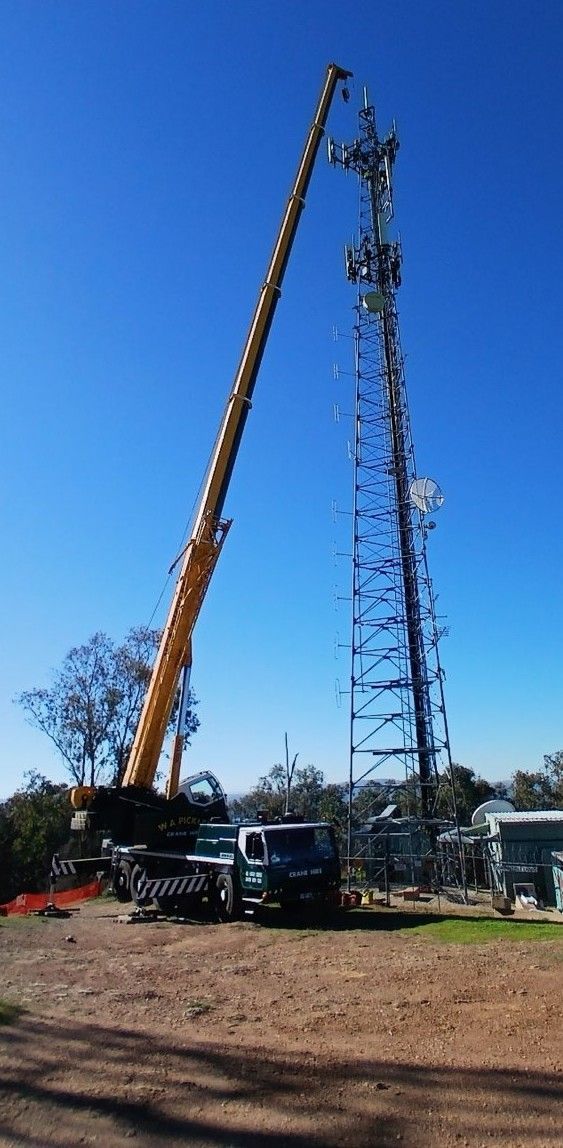 Yellow crane lifting a tall steel tower on a construction site under a clear blue sky