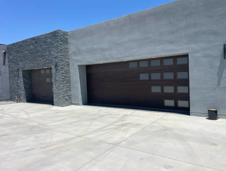 Two-car garage with brown doors and tan stucco exterior under a blue sky; a trailer sits in front.
