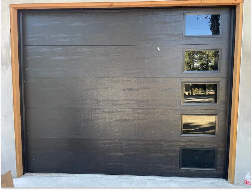 Black garage door with four rectangular windows and wood trim.