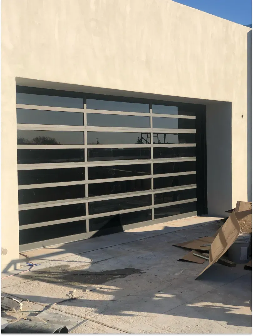 Garage door with horizontal panels, dark glass, and gray frame; set in a white stucco building.