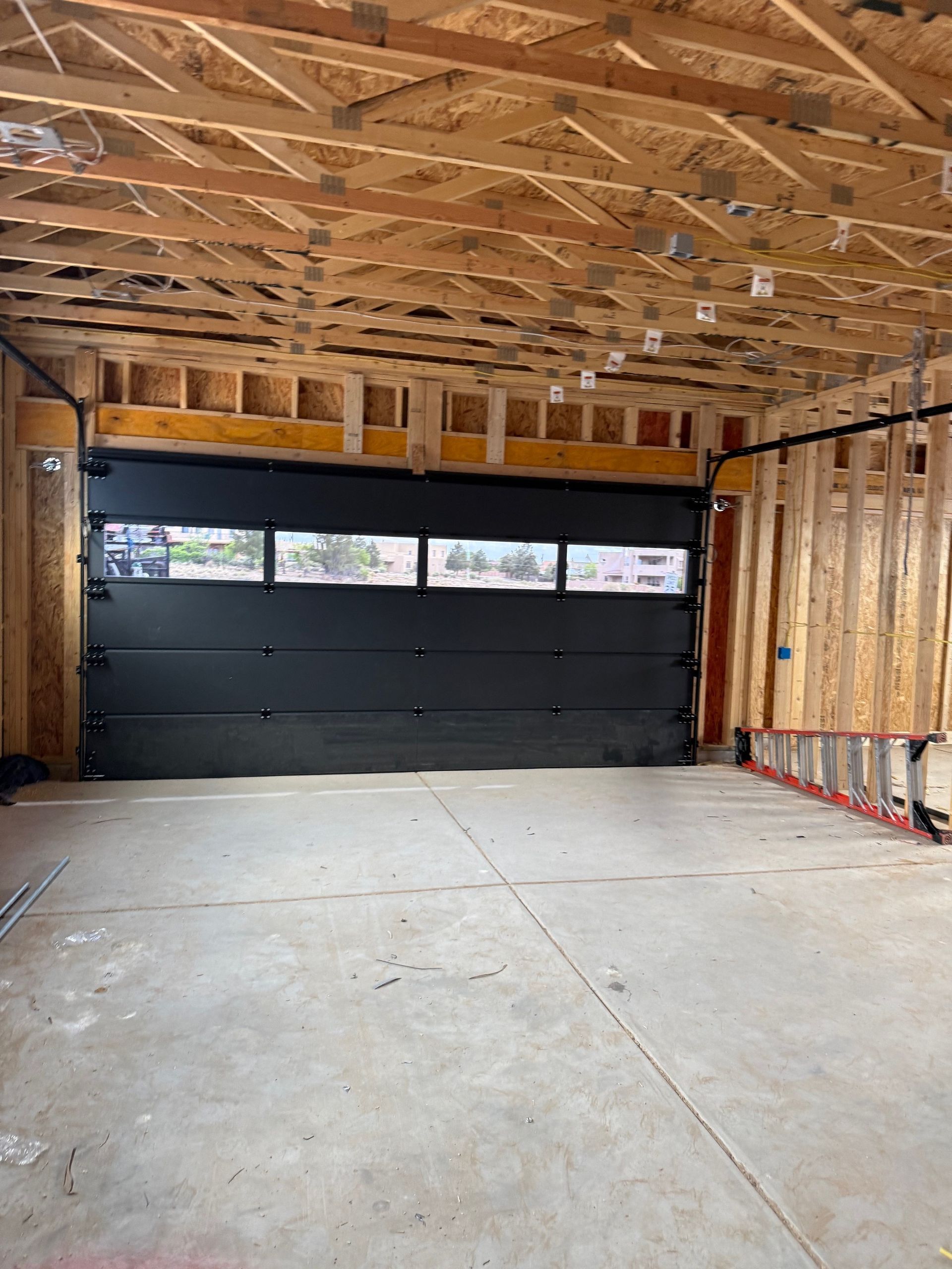 Empty garage interior with unfinished plywood walls, exposed rafters, and a closed black garage door.