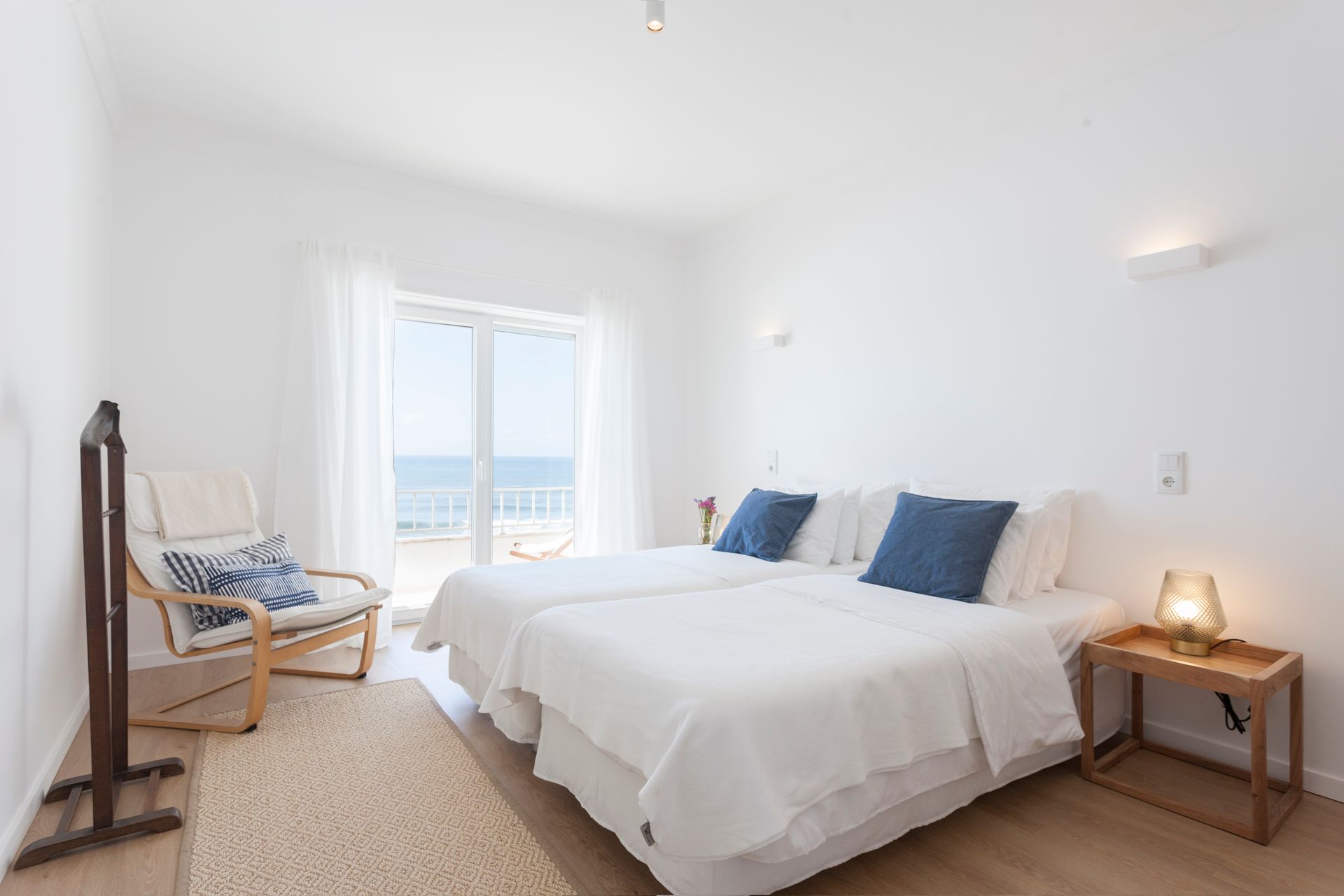 a bedroom with two beds and a chair with a view of the ocean .