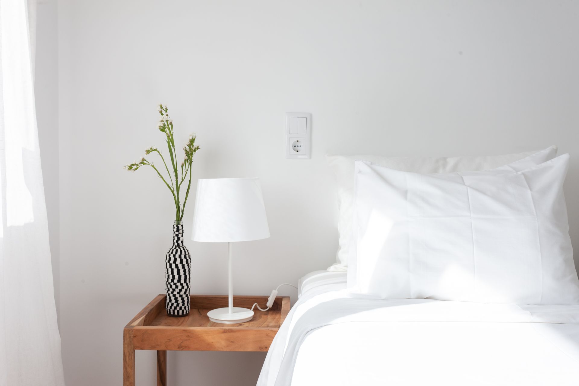 a bedroom with a bed , nightstand , lamp and vase of flowers .