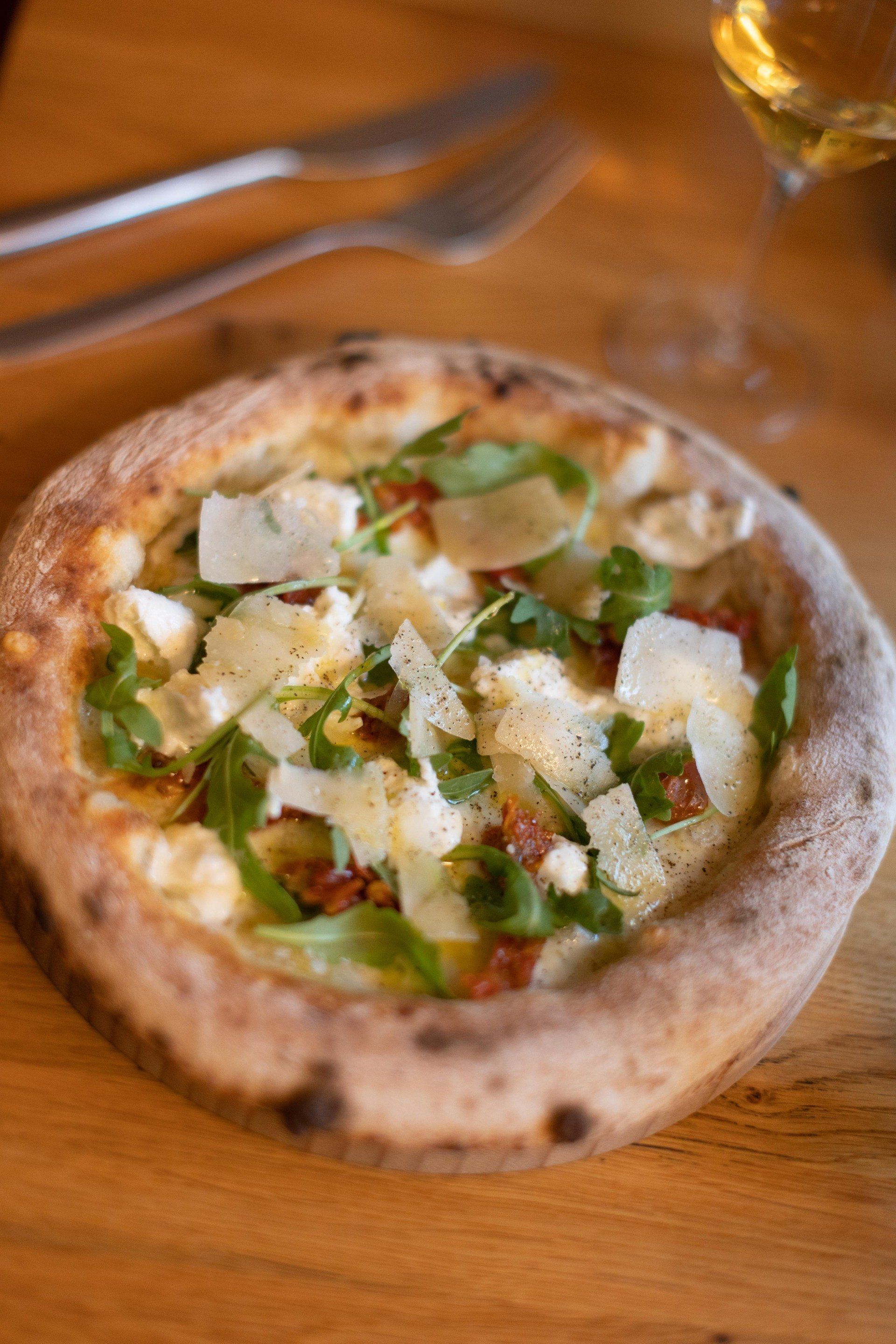 Une pizza est posée sur une table en bois à côté d'un verre de vin.