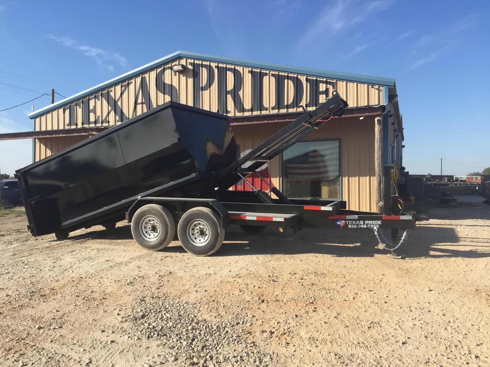 Black dump trailer parked on gravel in front of a building with a large 