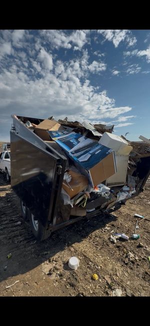Damaged metal container or vehicle wreckage in a rocky field under a cloudy blue sky